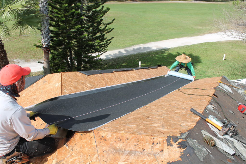 two roofers installing underlayment while working on a roof replacement